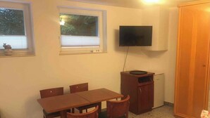 Une petite pièce avec une table et des chaises en bois, un téléviseur fixé au mur et une armoire.