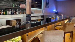 Uma área de bar com um balcão comprido, banquetas e prateleiras cheias de garrafas.