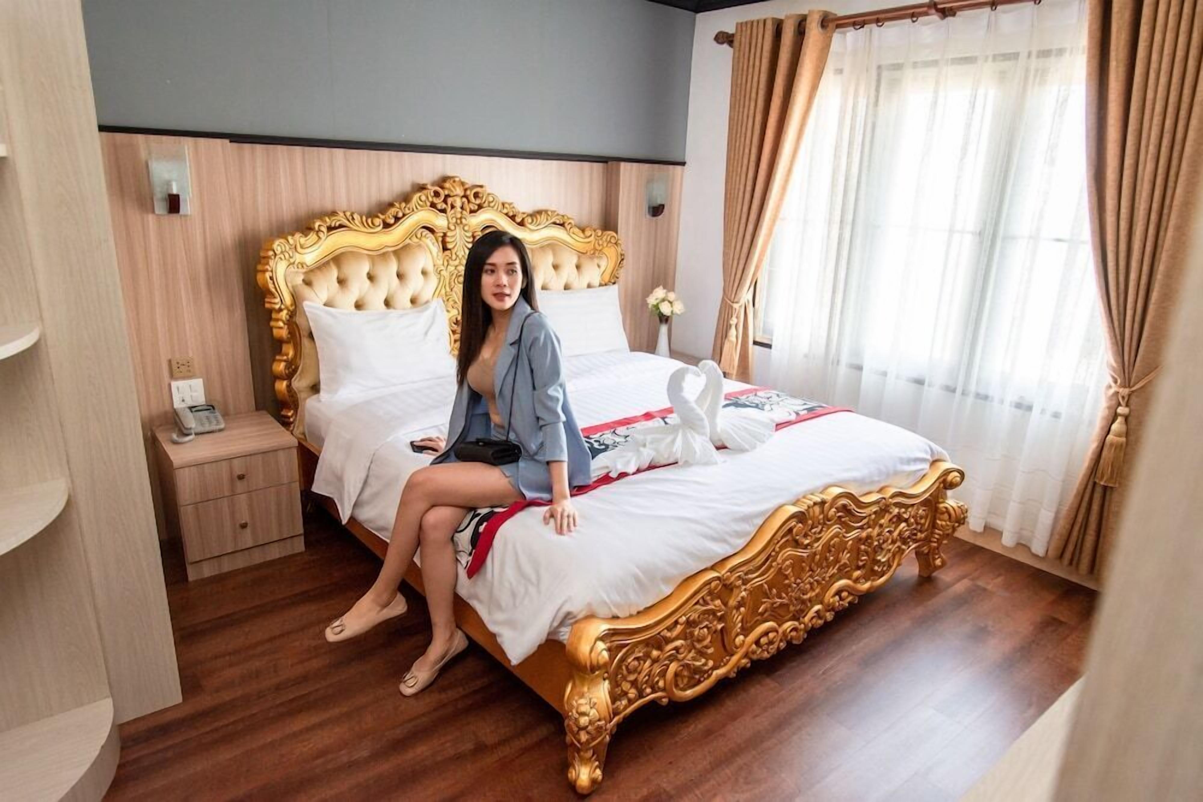 Una habitación con una cama grande y elaborada, una mesita de noche con un teléfono y una ventana con cortinas.