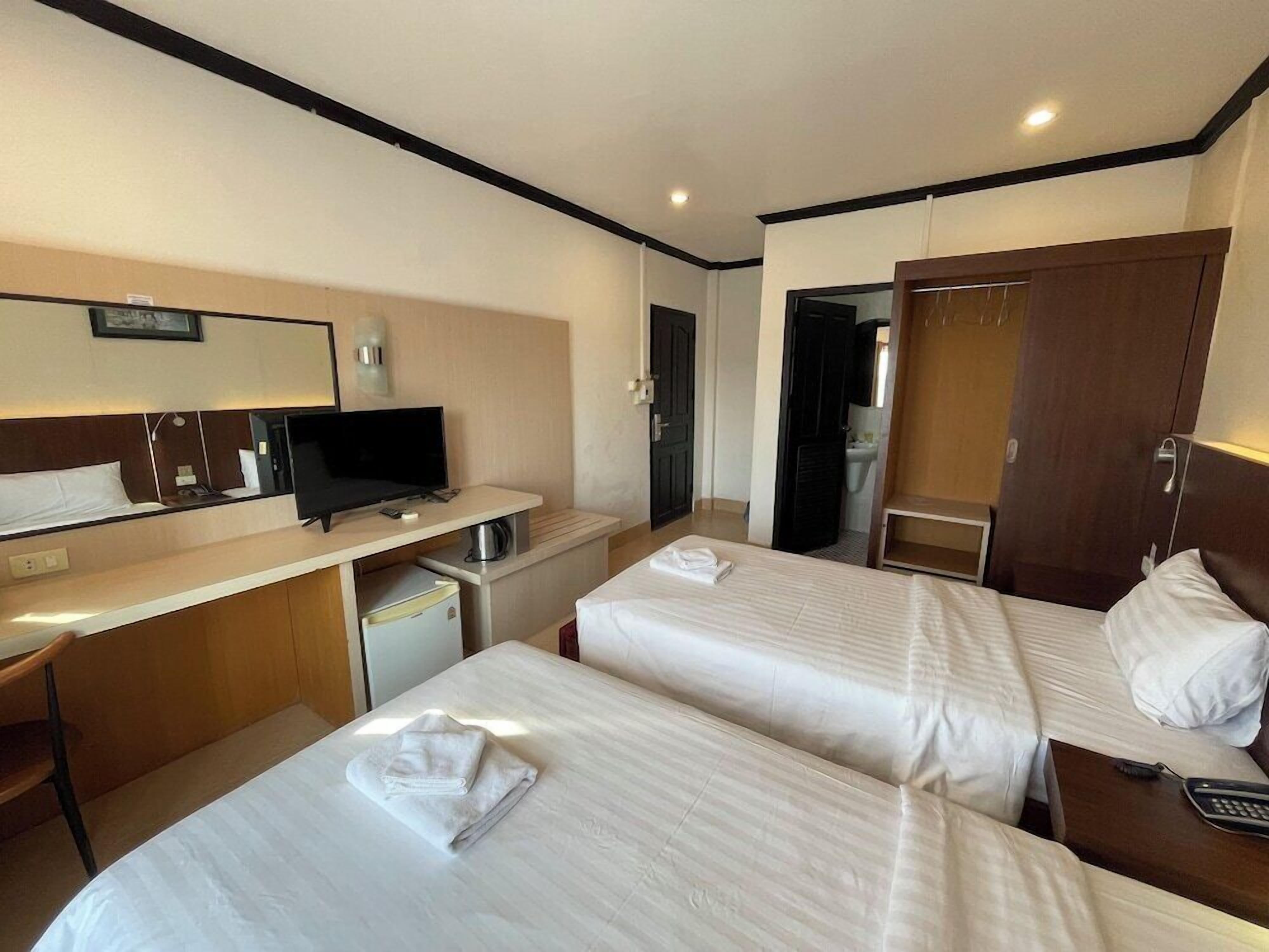 Habitación de hotel con dos camas, un escritorio con ordenador, un espejo y un armario.