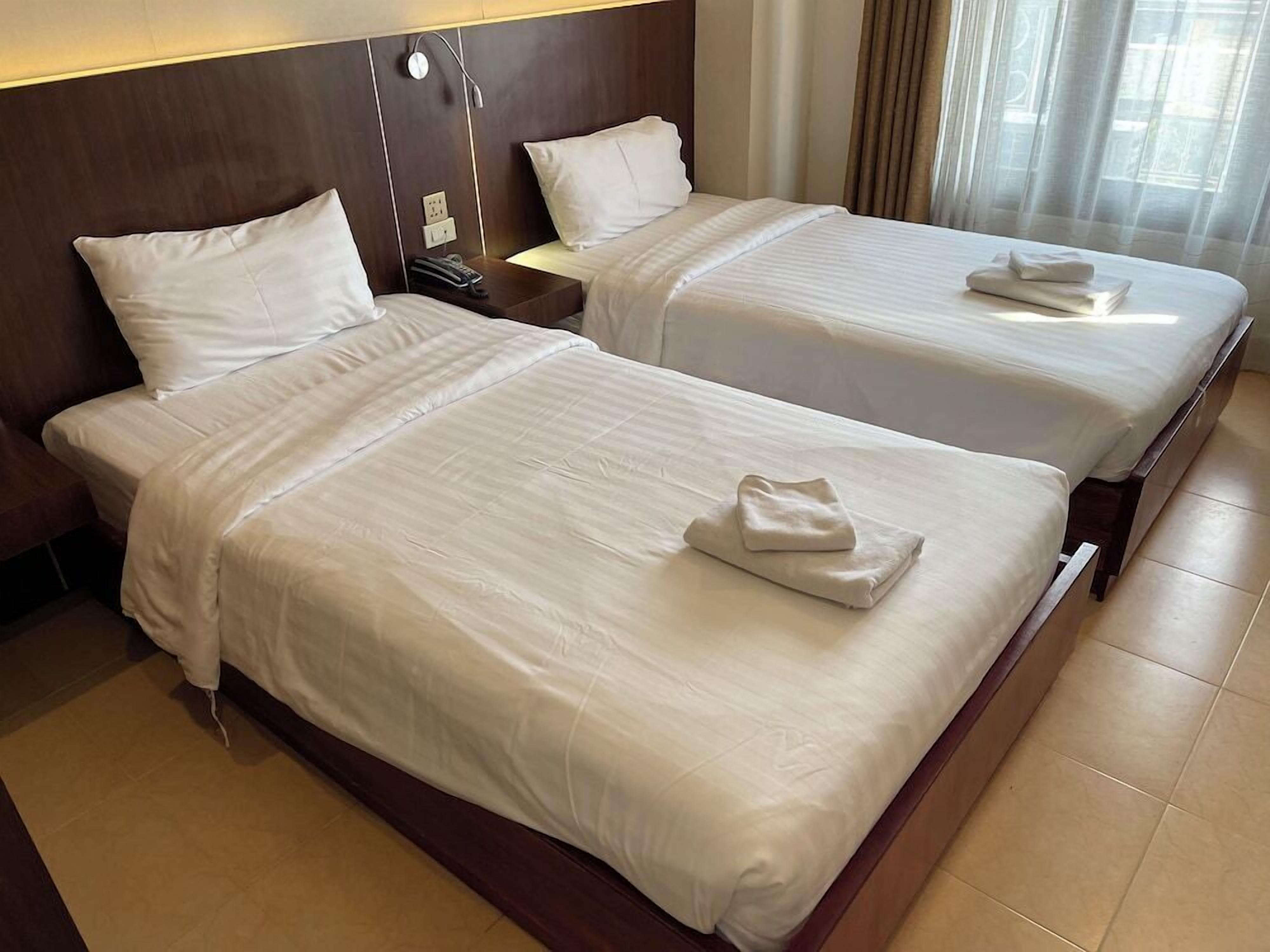 Ein Hotelzimmer mit zwei Betten, jeweils mit weißen Leinen und gefalteten Handtüchern.