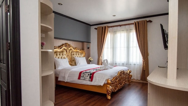 Quarto de hotel com uma cama grande, piso de madeira, TV fixada na parede e janela com cortinas.