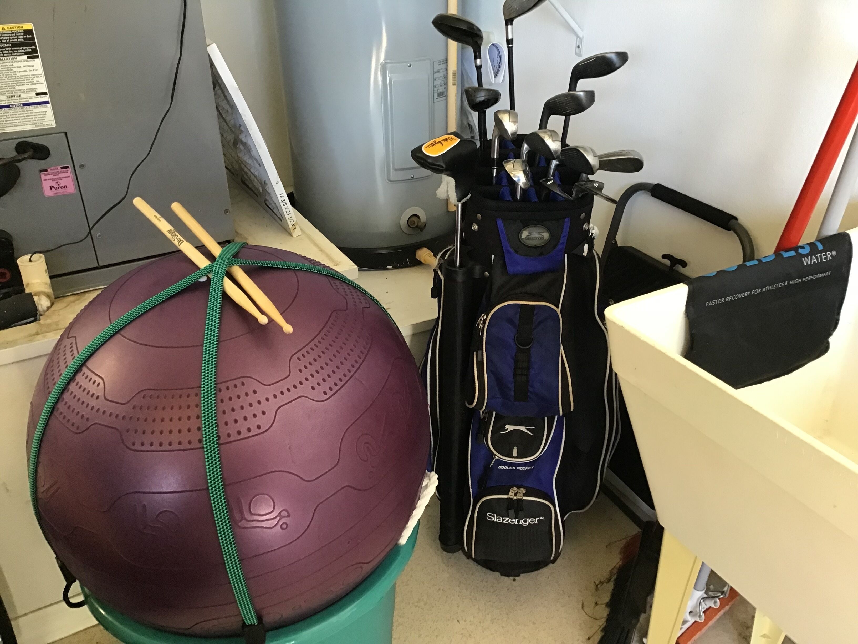 En lila träningsboll med ett grönt handtag, en blå golfväska och ett vitt skrivbord med ett rosa kort.