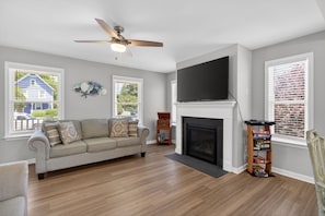A living room with a sofa, fireplace, TV, and windows. - Ocean Breeze - Chesapeake Properties (Cape Charles)