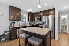 A modern kitchen with dark wood cabinets, stainless steel appliances, a granite countertop, and two bar stools. - Ocean Breeze - Chesapeake Properties (Cape Charles)