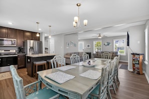 A modern kitchen with stainless steel appliances, a dining area with a large table and chairs, and a living area with a sofa and TV.