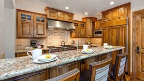 A kitchen with wooden cabinets, granite countertops, a stainless steel range hood, and a breakfast bar with chairs.