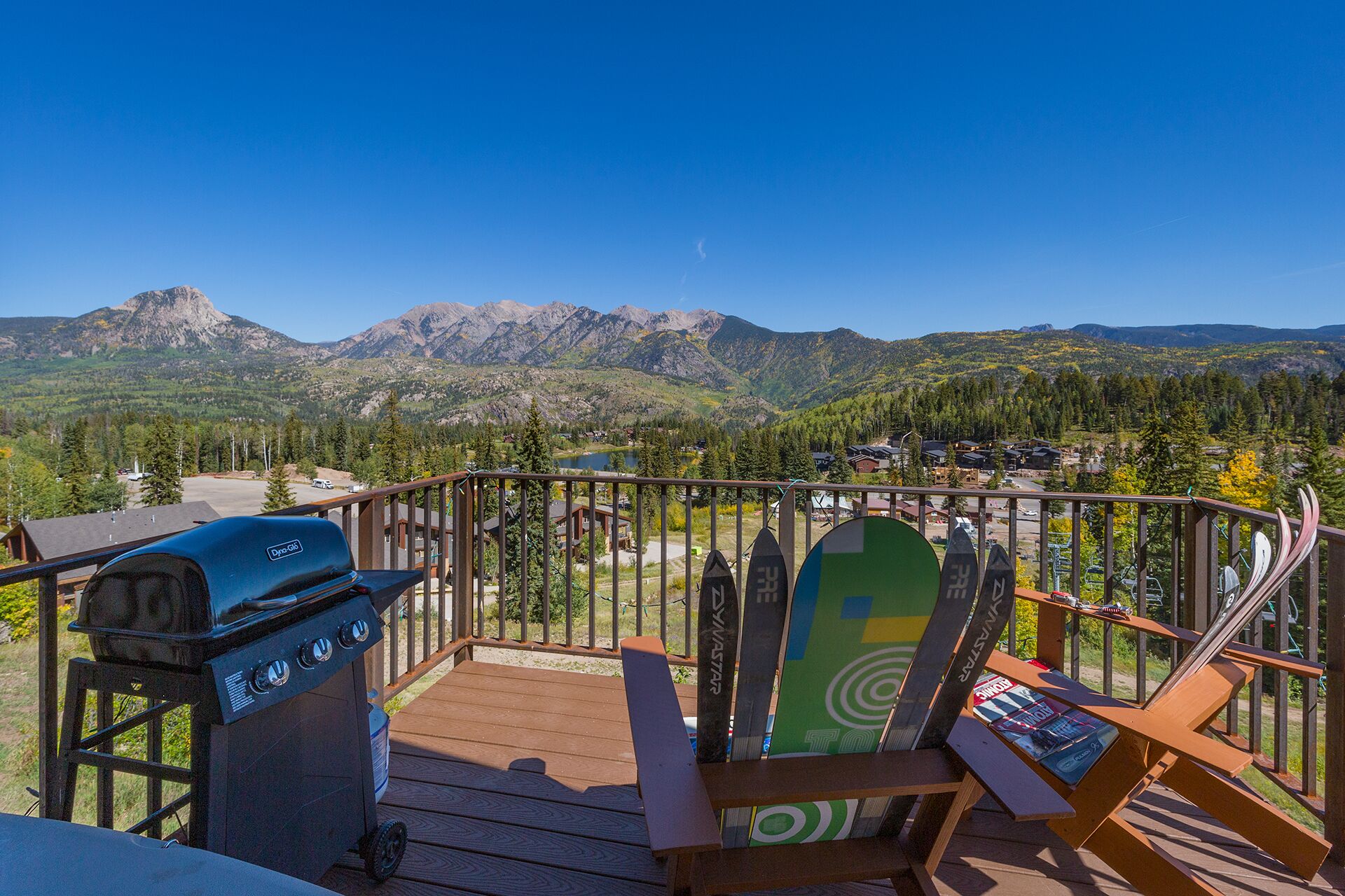 Eine Holzterrasse mit Grill und Schneebrettern, mit Blick auf eine gebirgige Landschaft.