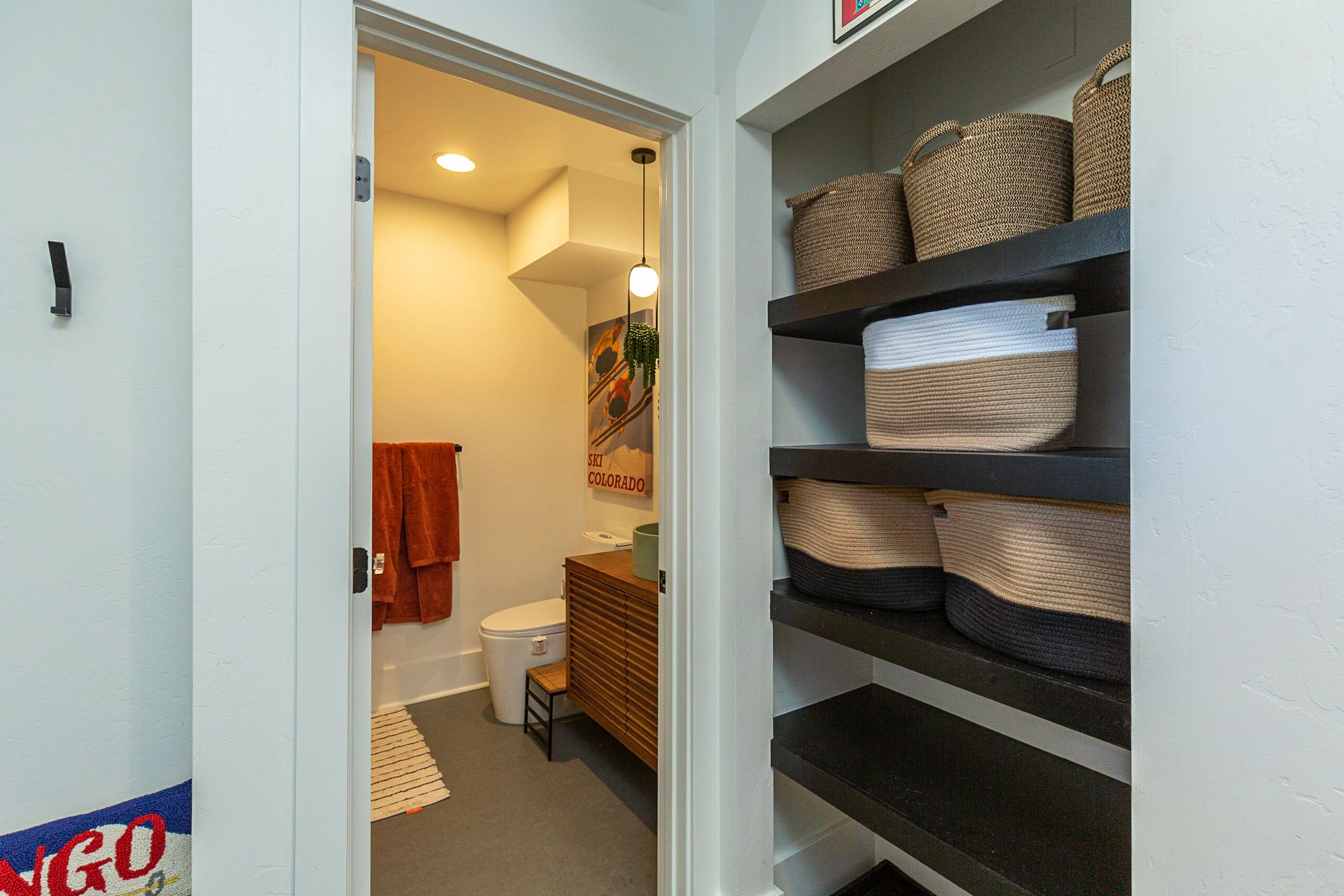 A bathroom with a toilet, sink, and towel rack. There are shelves with baskets and towels.
