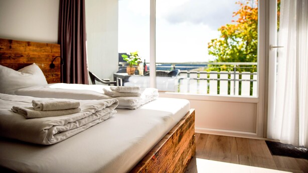 Une chambre d’hôtel avec un grand lit, une tête de lit en bois, un balcon avec vue sur les arbres et une balustrade.