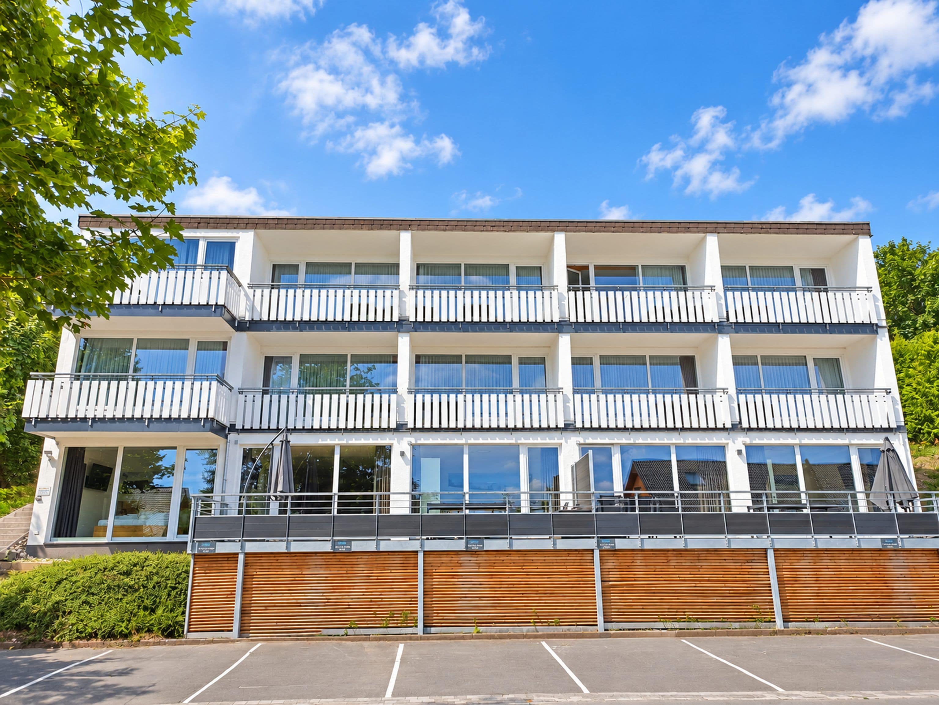 A multi-story building with balconies, large windows, and a parking area.