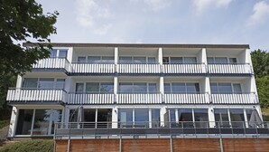 Un immeuble résidentiel à plusieurs étages, doté de balcons, de grandes fenêtres et d’un espace de stationnement à l’avant.