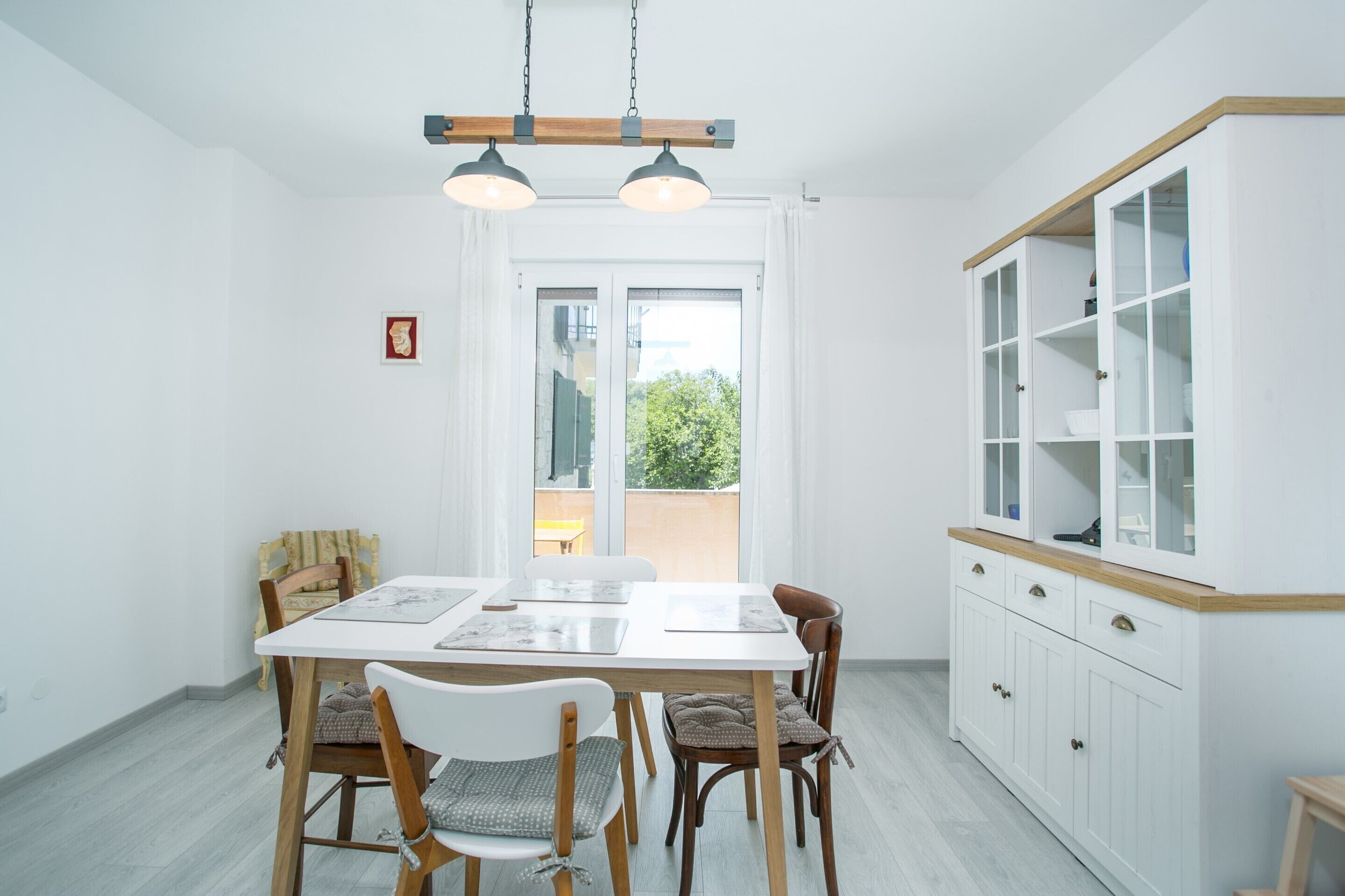 A bright dining area with a white table, wooden chairs, and a cabinet with glass doors.