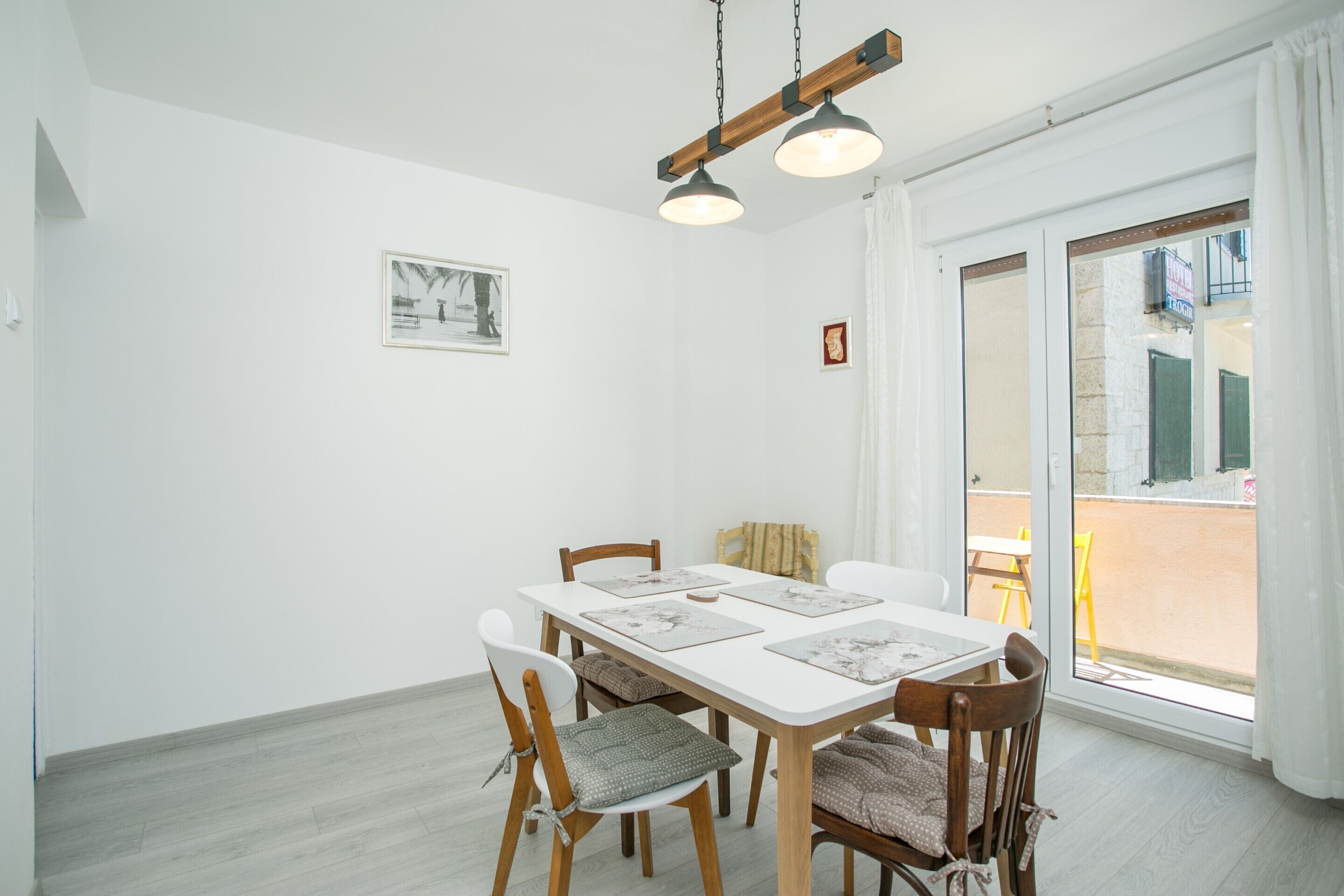A dining area with a white table and chairs, a hanging light fixture, and a view through a glass door.