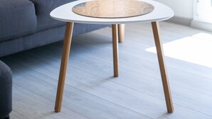 Ett modernt vardagsrum med en grå soffa, ett runt soffbord med en flätad skiva och en hög golvlampa.