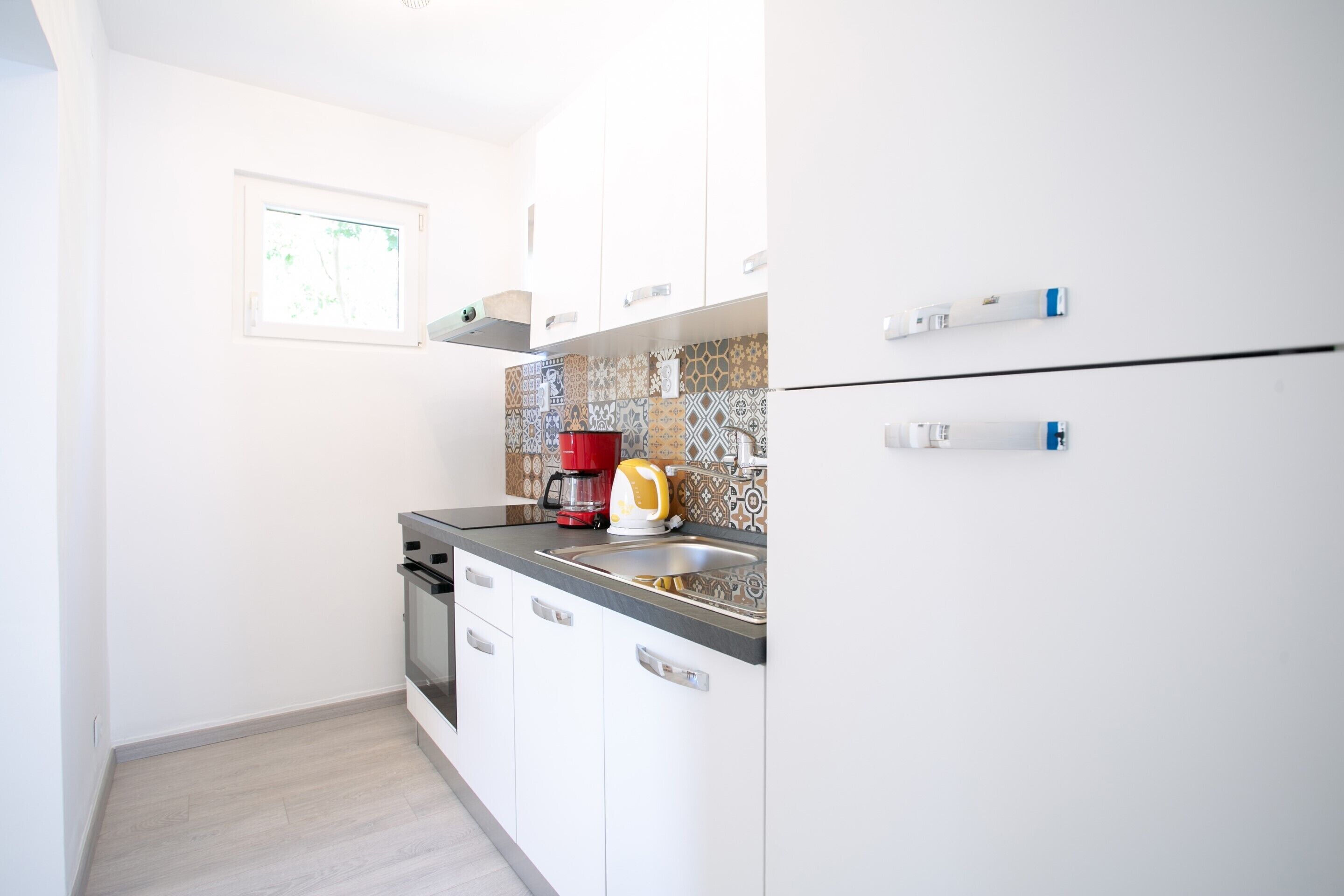 A small kitchen with white cabinets, a stainless steel sink, and a red coffee maker.