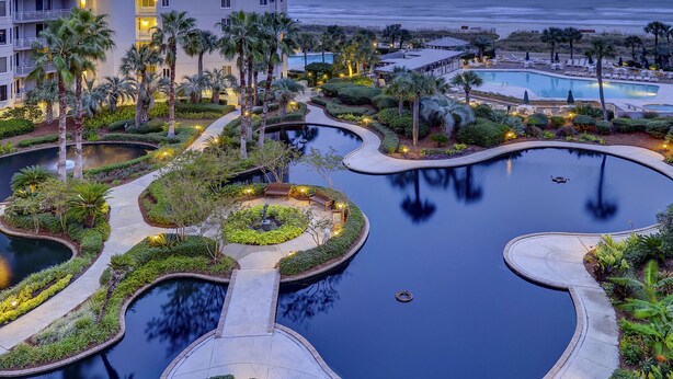 Ein Resort mit großem Poolbereich, Palmen und Blick auf den Ozean.