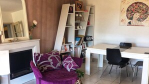 Una sala de estar con un sofá púrpura, un escritorio blanco, una estantería y una chimenea.