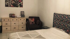 Un dormitorio con cama, cómoda, silla y cabecera de pared con estampado floral.