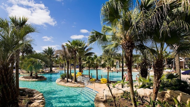 Ein Poolbereich eines Resorts mit mehreren Pools, Palmen und Liegestühlen.