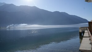 A lake with mountains in the background, a clear sky, and a wooden dock extending into the water. - Feet in the water! (Duingt)