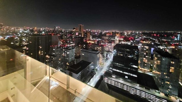 Panorama nocturno de la ciudad desde un punto elevado, con edificios iluminados y una calle concurrida abajo.