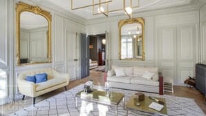 Ein geräumiges Wohnzimmer mit zwei weißen Sofas, einem Couchtisch und großen, goldfarbenen Spiegeln.