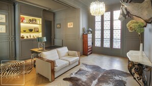 Ein Zimmer mit einem weißen Sofa, einer Kristallleuchtre, einem aufgehängten Hirschkopf und einem gemusterten Teppich.
