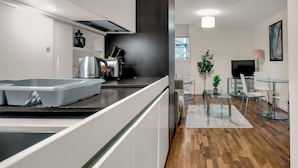 A modern kitchen with white cabinets, a black countertop, and a dining area with a glass table and chairs. - One Bed Serviced Apt Moorgate (London)