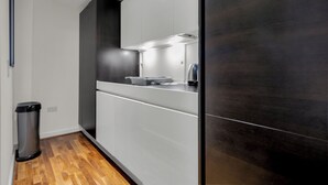 A modern kitchen with white cabinetry, a stainless steel trash can, and a wooden floor. - One Bed Serviced Apt Moorgate (London)