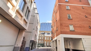 A narrow street between buildings with a mix of modern and traditional architecture, including a red brick building and a glass skyscraper in the background. - One Bed Serviced Apt Moorgate (London)
