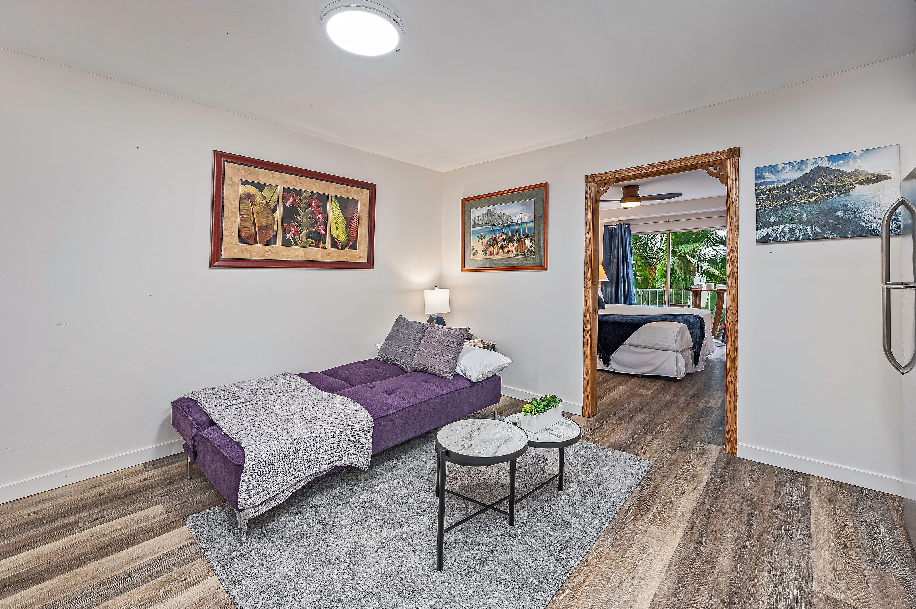 Une chambre à coucher moderne avec un lit violet, une petite table ronde et une vue sur un balcon.