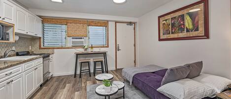 A compact living space with a kitchenette, a dining area, a sofa, and a framed artwork on the wall.