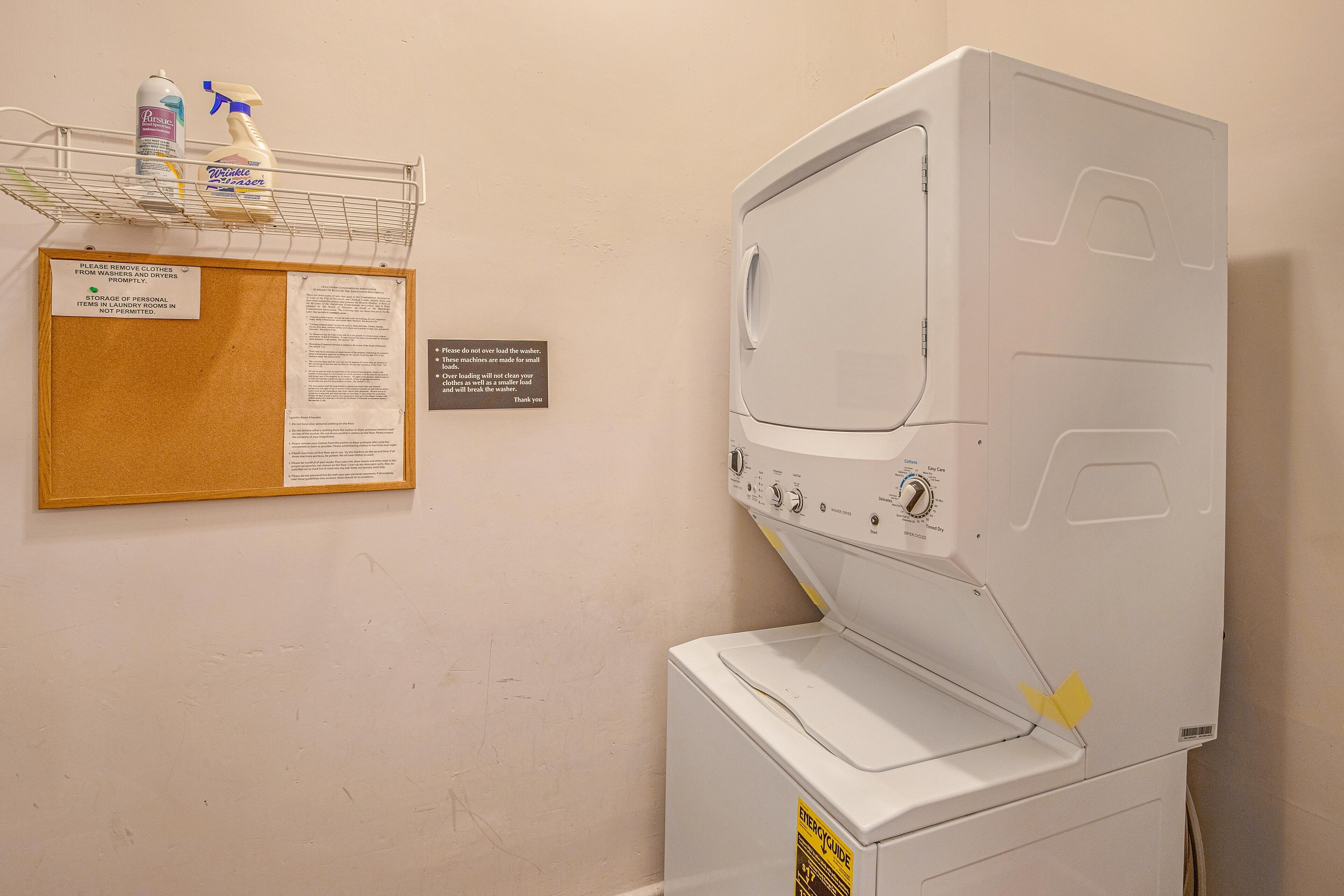 Una lavadora de carga frontal con panel de control, una pizarra con normas para el lavadero y un estante con productos de limpieza.