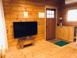 Cozy cabin interior with a flat-screen TV, wooden table, and a view of the outside.