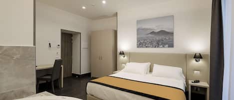 A modern hotel room with a large bed, a desk, a chair, a desk lamp, a nightstand, and a wall-mounted lamp.
