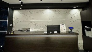 Un comptoir d’accueil avec un mur en marbre en arrière-plan, un écran numérique et une caméra de surveillance au-dessus.