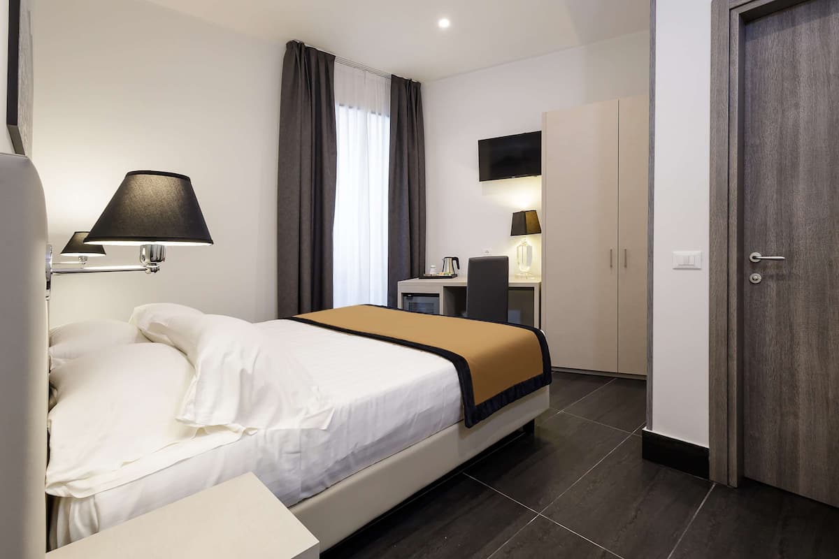 A hotel room with a bed, a desk, a chair, a TV, and a wardrobe.