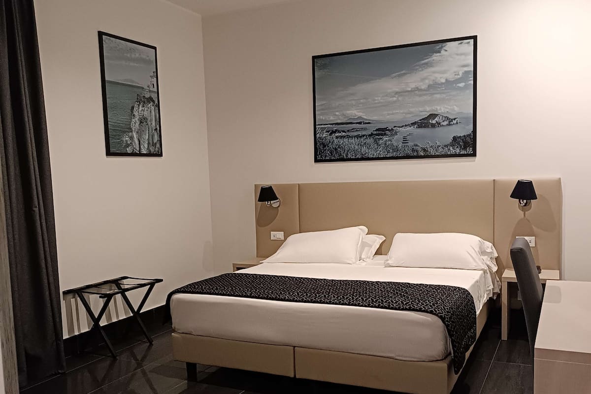 A modern hotel room with a large bed, a desk, a chair, and two framed pictures on the wall.