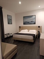 Una camera d'albergo moderna con un letto grande, una scrivania, una sedia e due quadri appesi al muro.