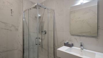 A modern bathroom with a glass-enclosed shower, a white sink, and a large mirror.