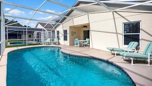 A pool area with a covered patio, lounge chairs, and a clear sky.