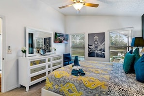 A bedroom with a bed, a dresser, a ceiling fan, and artwork on the walls.