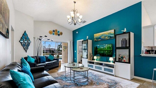A modern living room with a black leather sofa, teal cushions, a glass coffee table, and a teal accent wall.