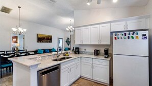 A modern kitchen with white cabinets, a dishwasher, a refrigerator with magnets, and a dining area with blue chairs.