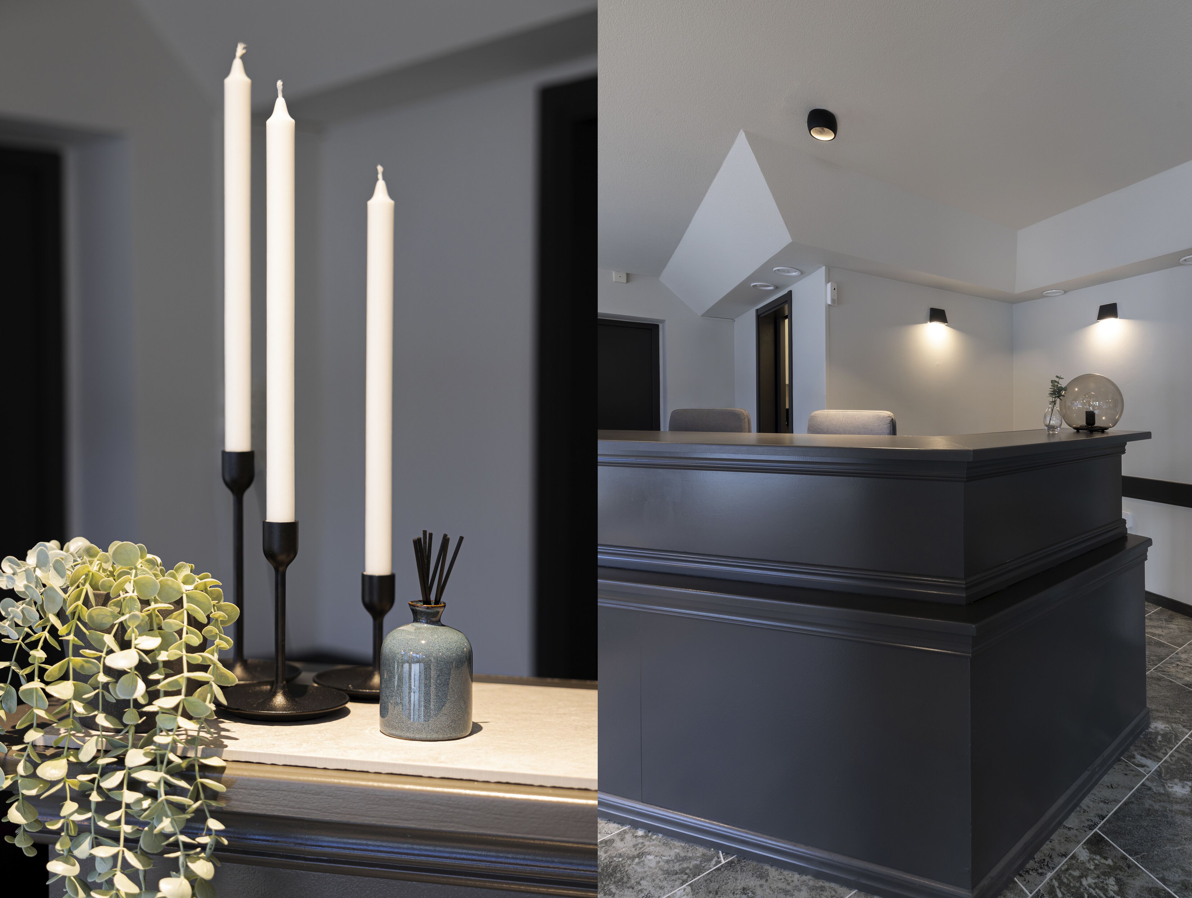 En moderne receptionsdisk med mørk finish, to høje hvide lys, en vase med grønne planter og et geometrisk lysarmatur i loftet.