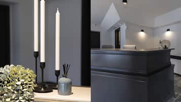 En moderne receptionsdisk med mørk finish, to høje hvide lys, en vase med grønne planter og et geometrisk lysarmatur i loftet.