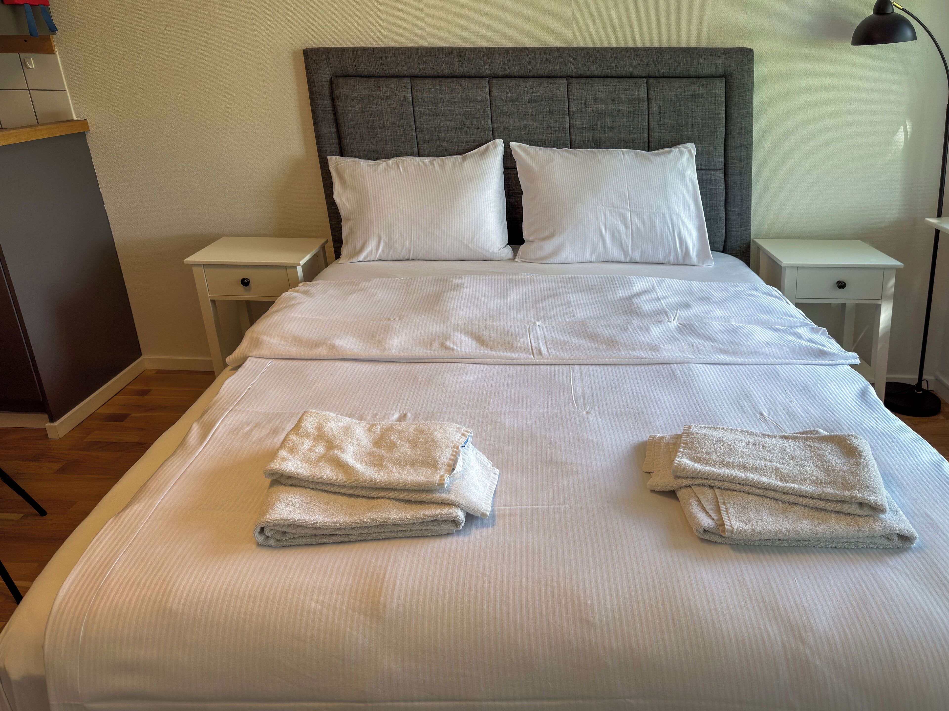 Una cama bien hecha con sábanas blancas y dos toallas dobladas encima.
