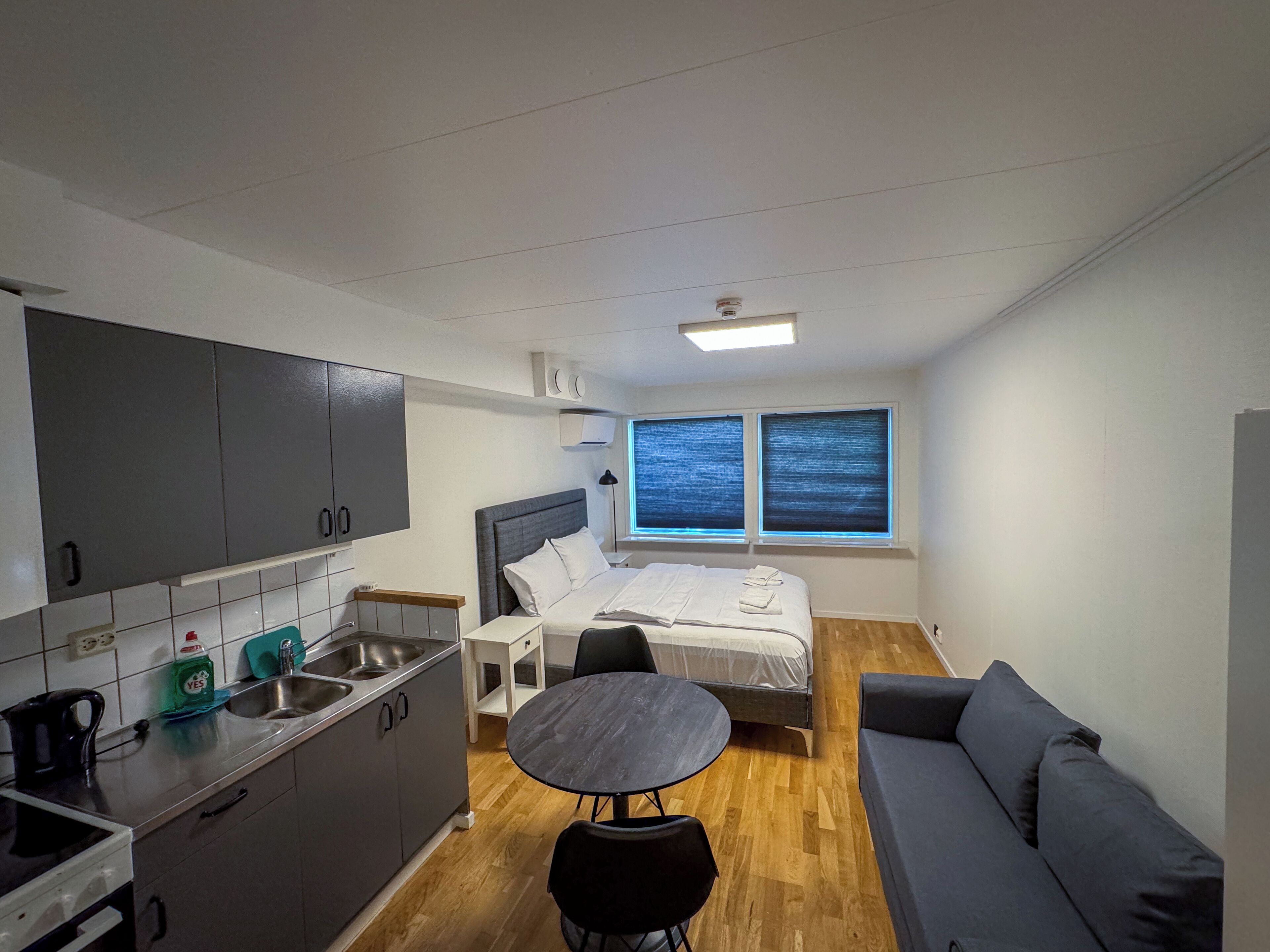 A compact room with a kitchenette, a bed, a small table, and a sofa.