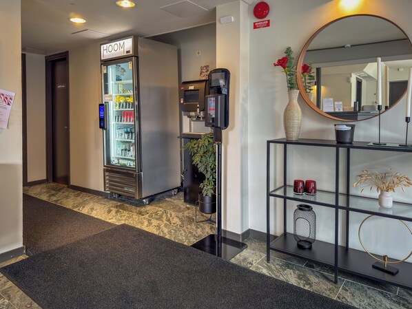 A hotel lobby with a self-service beverage machine, a staff room, and a reception desk with a mirror and decorative items.